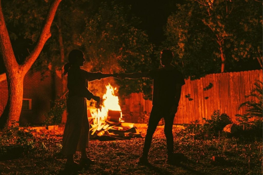 a couple holding hands in front of a bonfire in a yard
