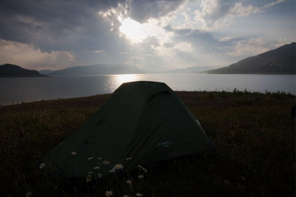dark tent next to white flowers by a lake