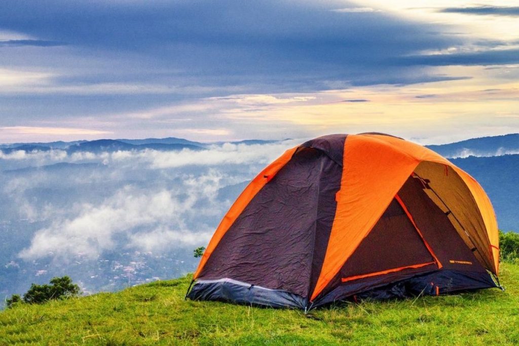 purple and orange tent on a grassy hill above the clouds