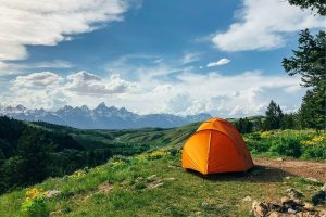 orange tent on a grassy hill with mountains in the distance
