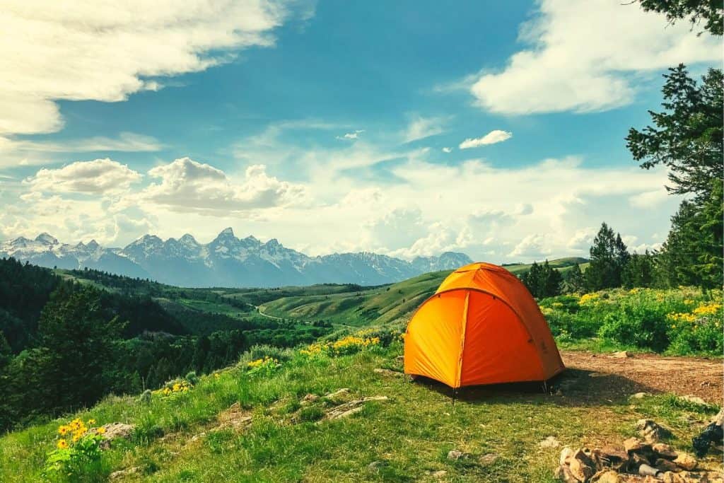 orange tent grassy hill mountains and blue sky