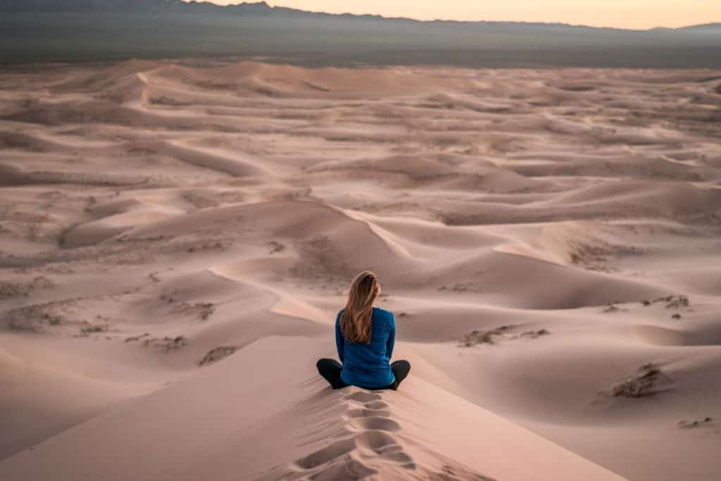 woman in blue shirt sitting on sand in dunes