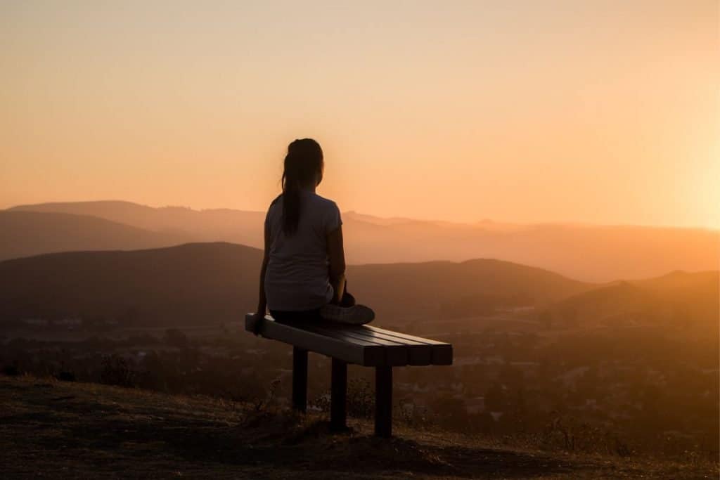 woman sitting on bench at sunset in mountains