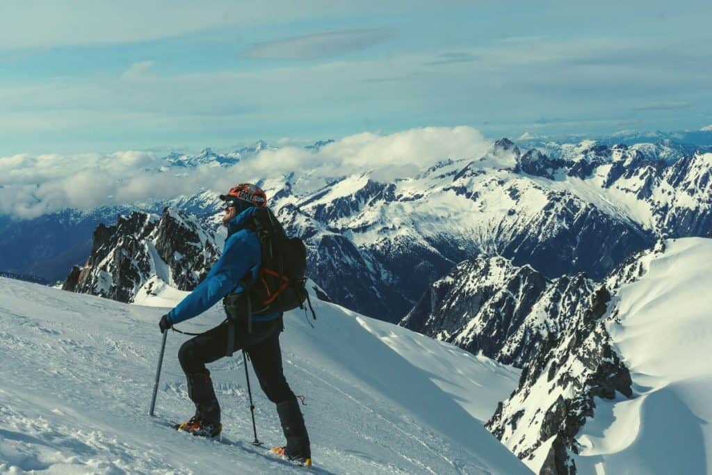 man in blue coat hiking up a snowy mountain