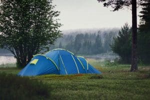 large blue tent on grass with trees and water