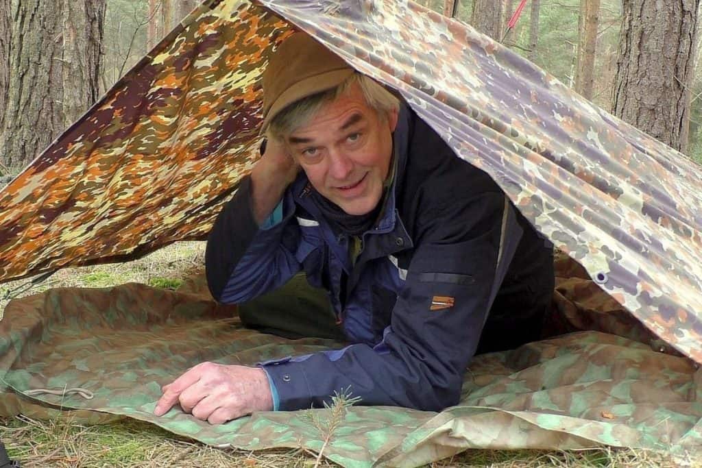 man lying under a camo tarp on top of a groundsheet