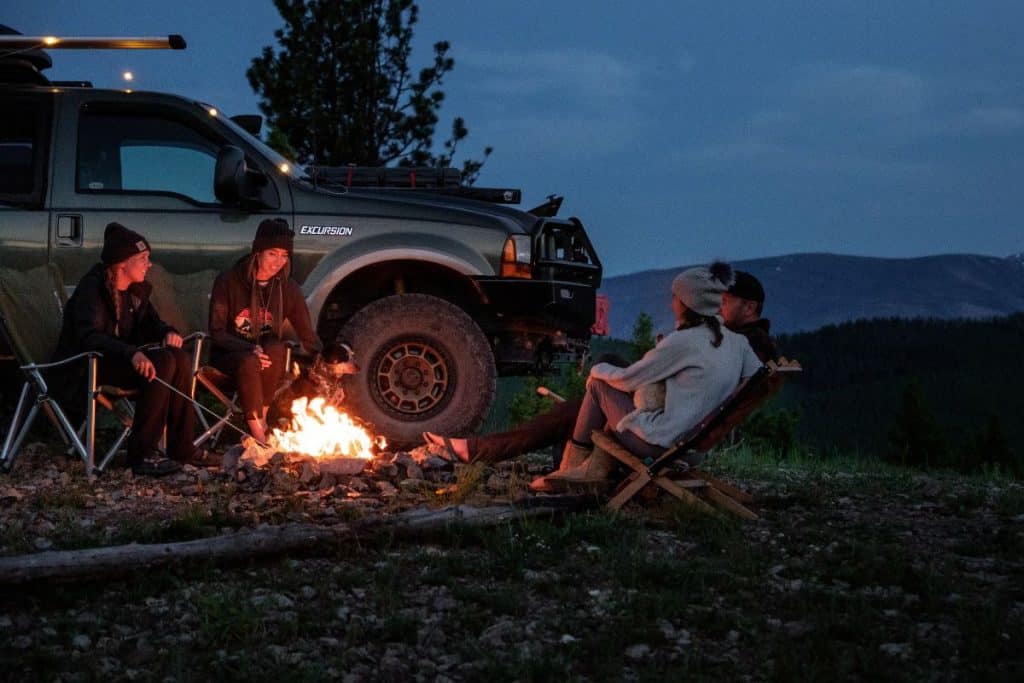 people sitting around a campfire next to a truck