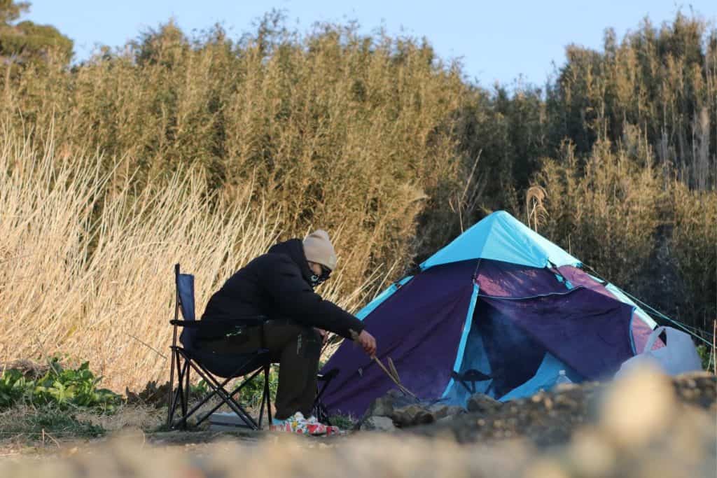 person sitting on a chair next to a purple ten tending a fire