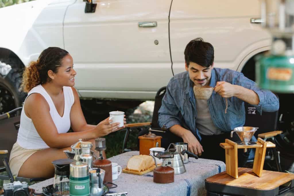 a man and woman sitting around a table outside eating breakfast by a truck