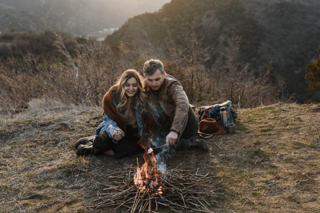 man and woman snuggling by a campfire