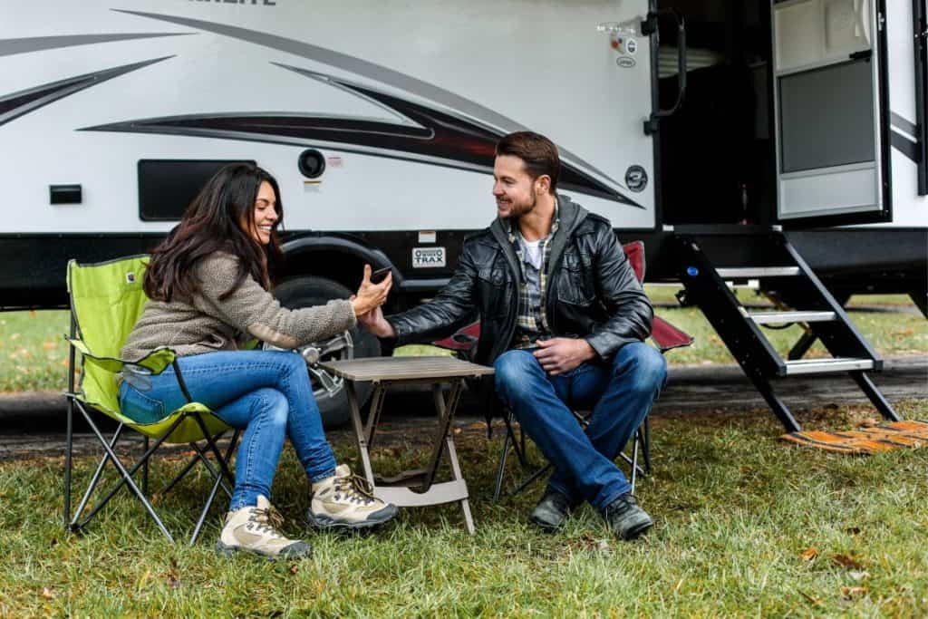 man and woman sitting in camping chairs next to an rv