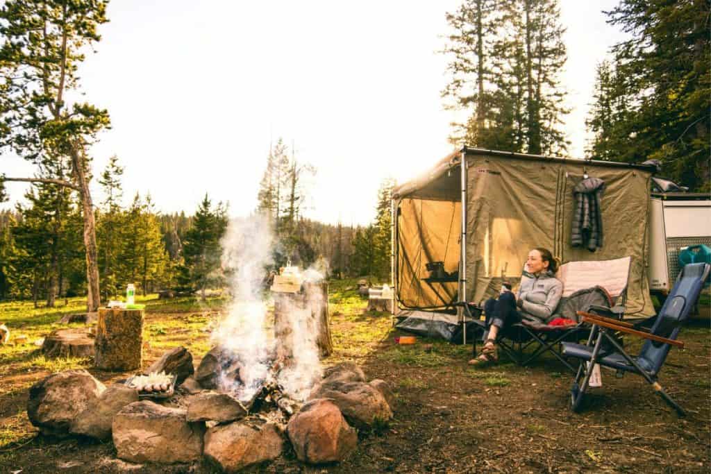 woman sitting in a chair next to a tent and fire pit