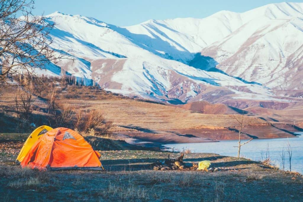 orange and yellow tent by lake and mountains