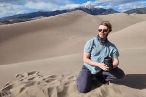 man kneeling in the sand with a campfire cooking kit