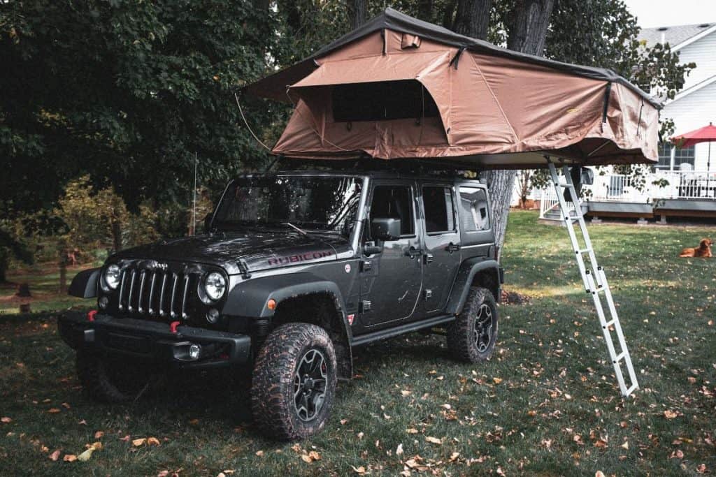 jeep with rooftop tent and ladder in a yard