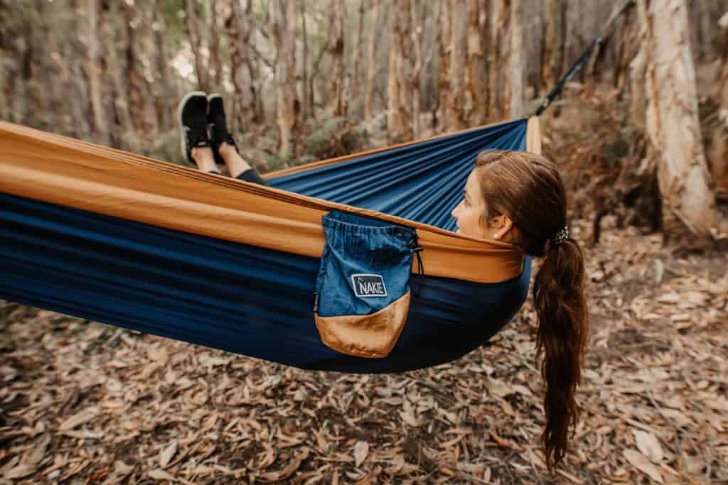 woman lying in an orange and blue hammock in the forest