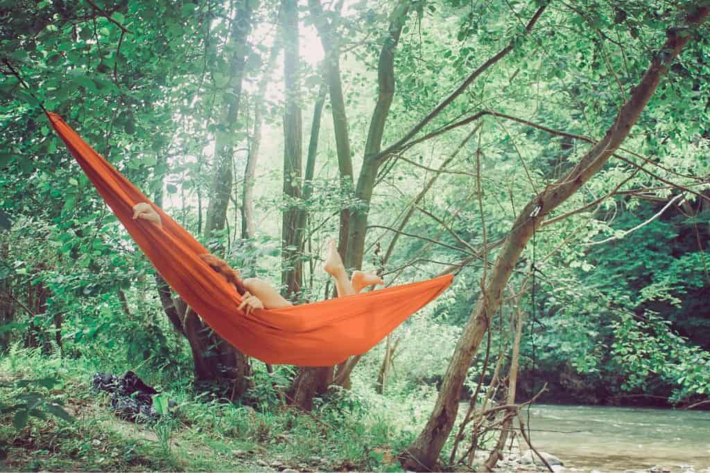 orange hammock with woman in trees by water