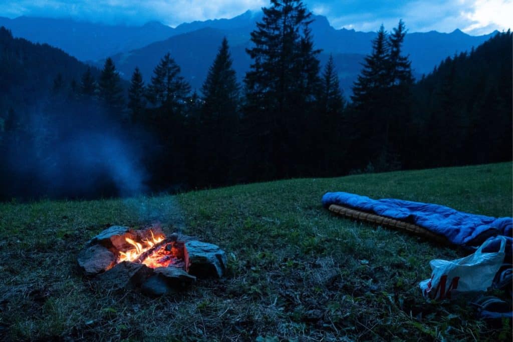 campfire at twilight in the mountains with two sleeping bags
