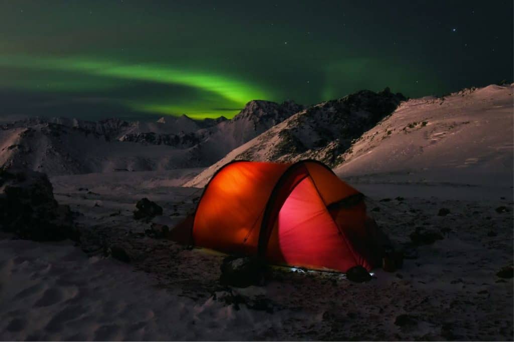 red tent on snowy mountain with northern lights