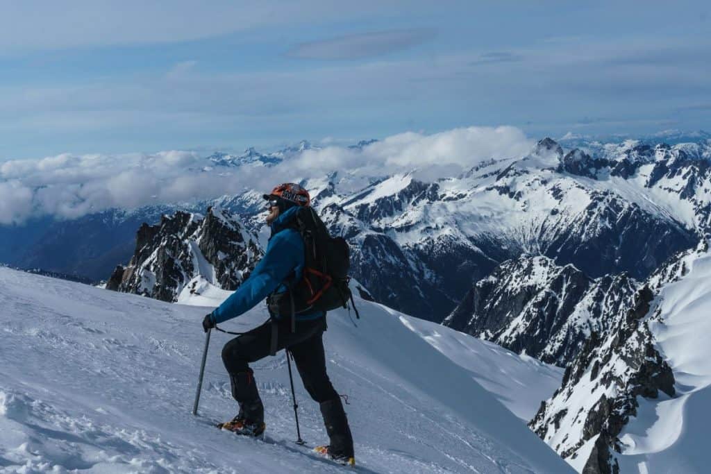 man in blue jacket hiking up a snowy mountain slope
