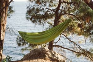 green hammock hung between two trees by the water