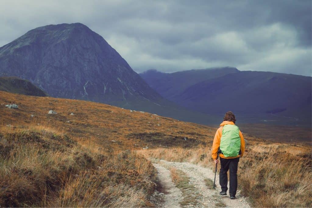person walking with a green backpack through a mountain trail