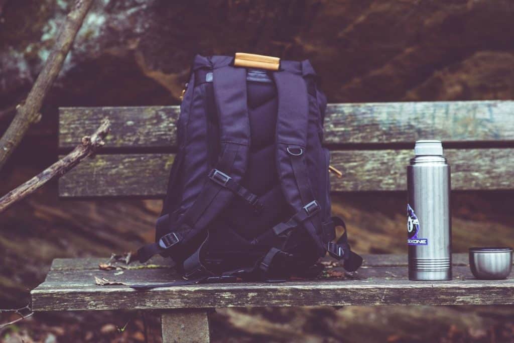 purple backpack sitting on a bench by a thermos