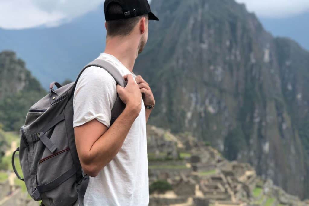 man in white shirt and black hat carrying a backpack in the mountains