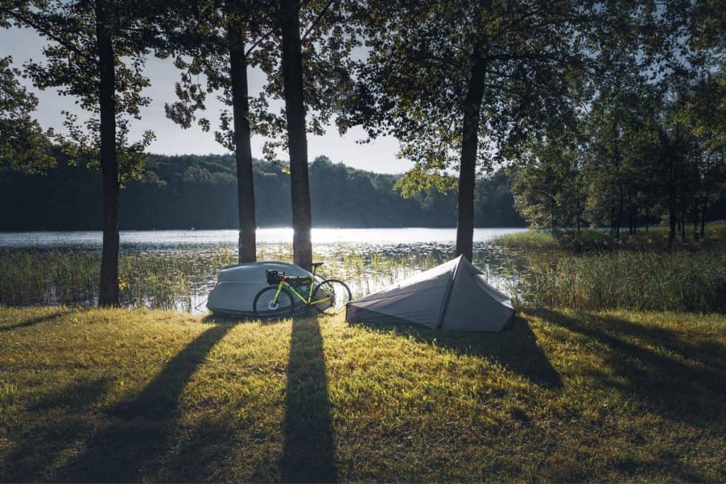 bike, tent, and boat on grass by a lake