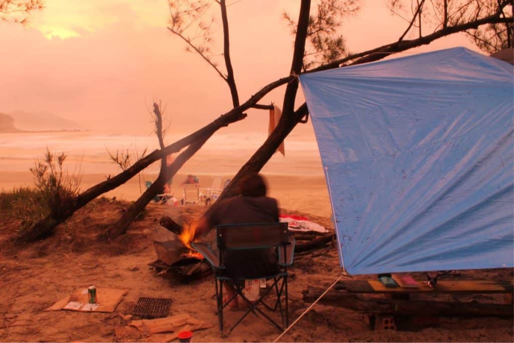 man sitting on the beach with a blue tarp and firepit