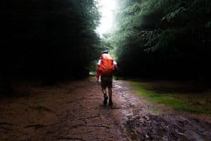 man with orange backpack hiking down a muddy road