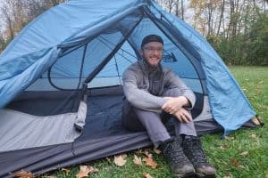 man sitting in a blue tent while wearing a gray jacket