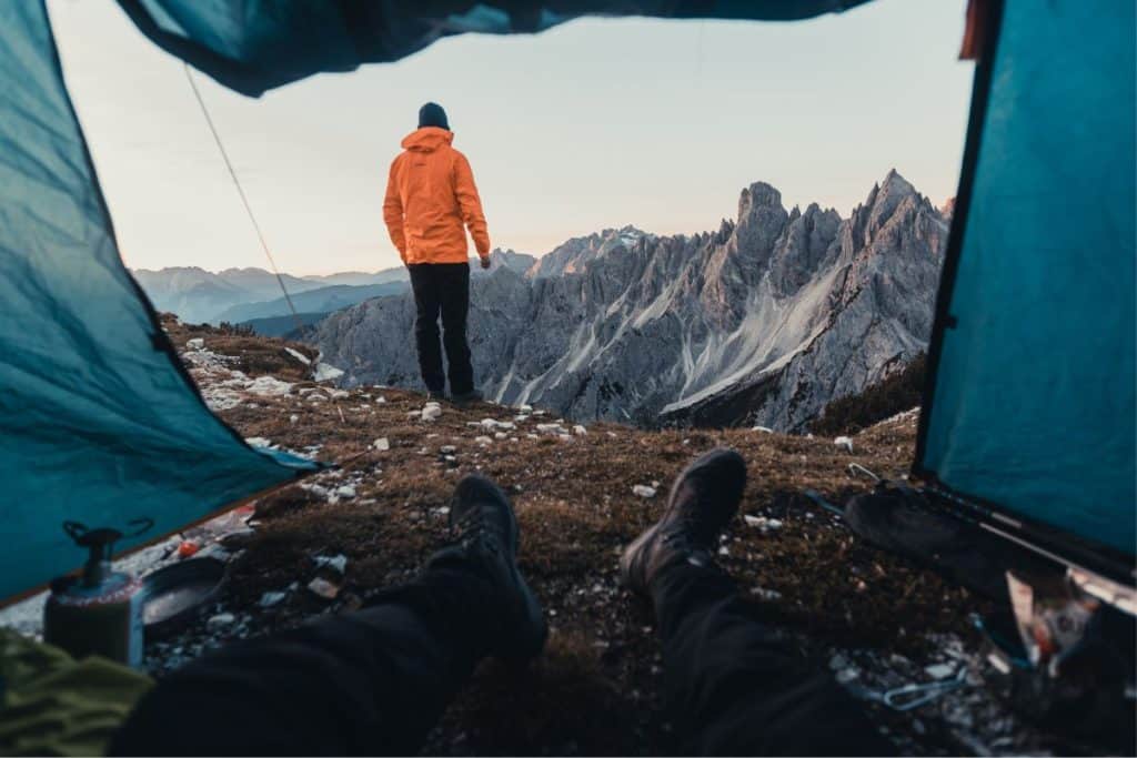 blue tent man in orange jacket standing on mountain range