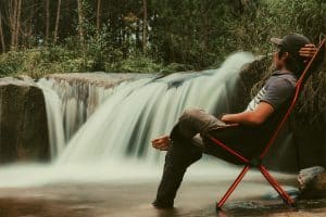 man sitting in a camping chair by a waterfall