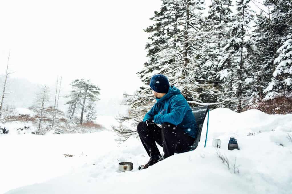 man in blue coat sitting in a chair in snow