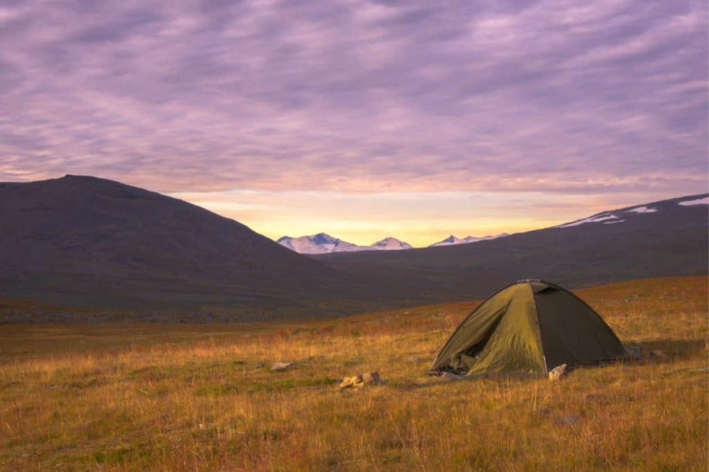green tent on grass by hills at sunset