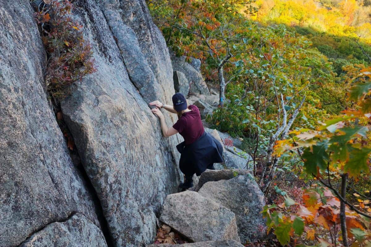 woman in red shirt climbing down the side of a cliff