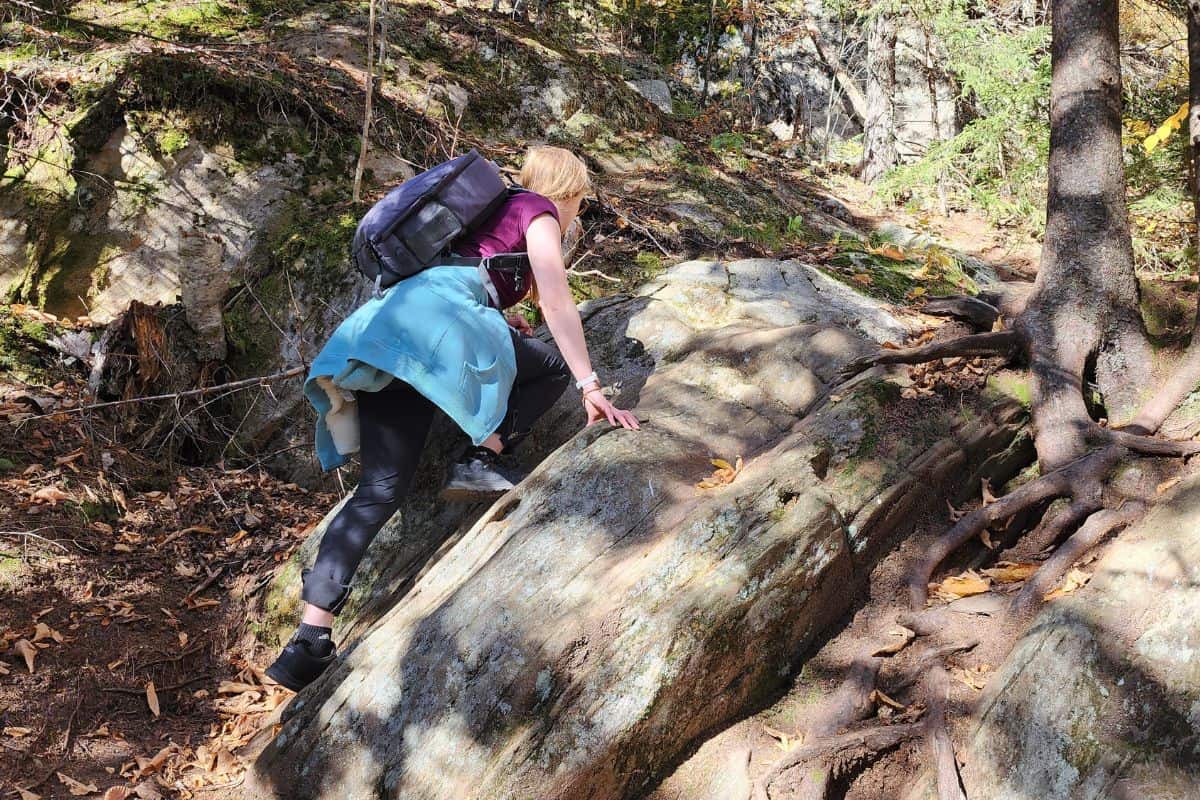 woman with blue sweatshirt climbing up a rock