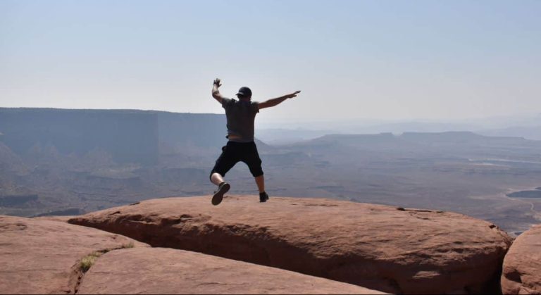 man jumping over a cliff on red rock
