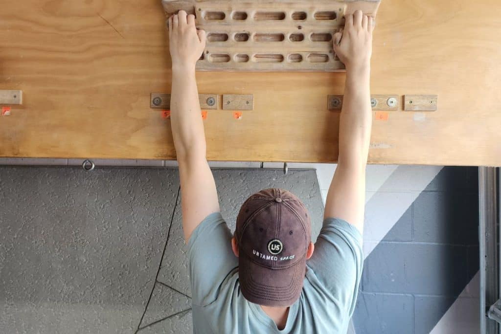 man hanging from a hangboard with a hat on