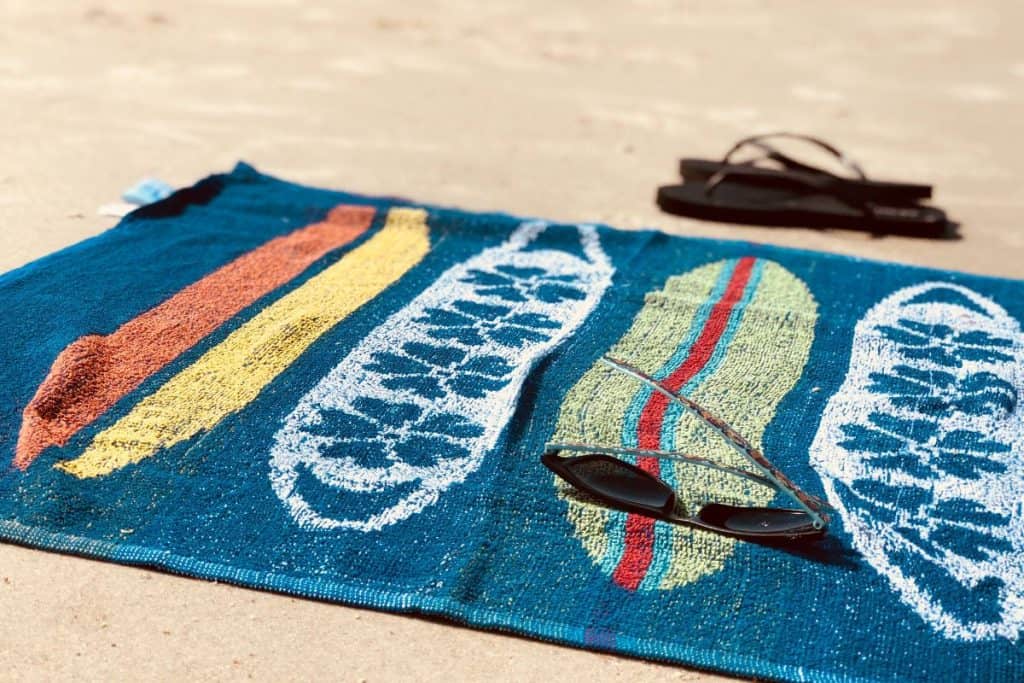 blue towel with sunglasses and flip flops on the beach