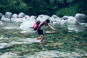 man crossing a river with a backpack on
