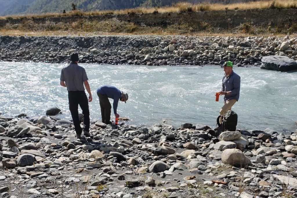 three men getting water from a river