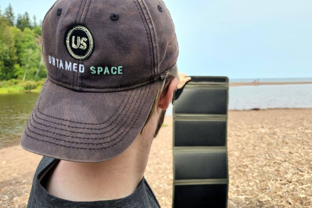 man wearing an untamed space hat holding a backpacking solar panel