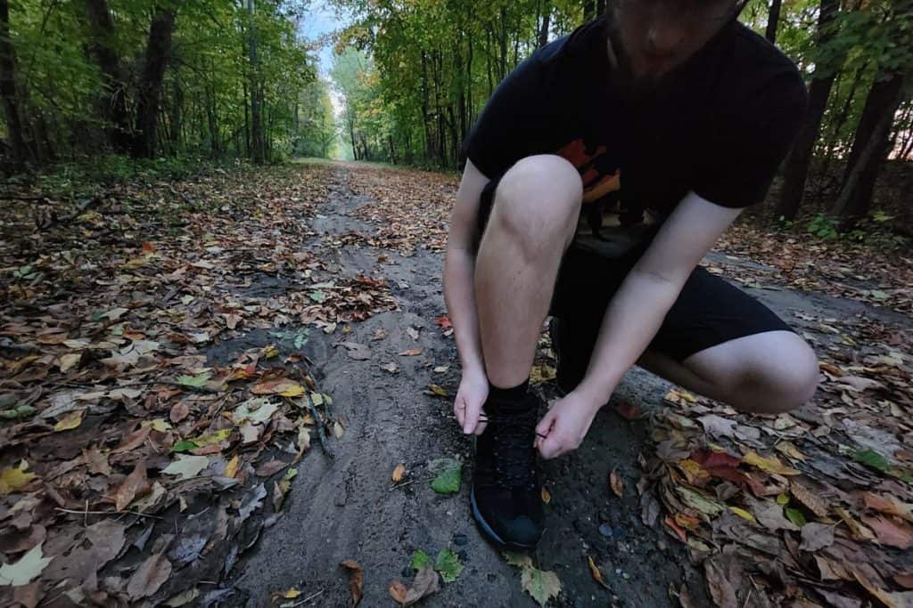 man squatting to tie boots on a dirt trail