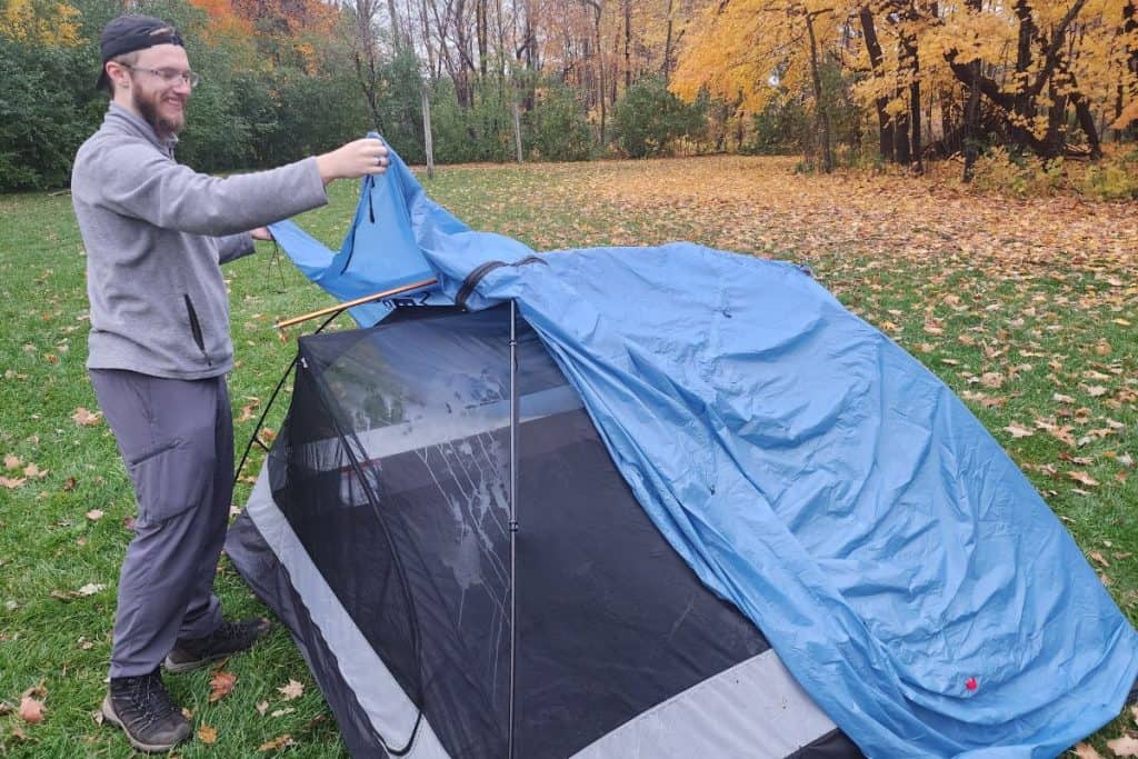 man putting a blue rainfly on a tent