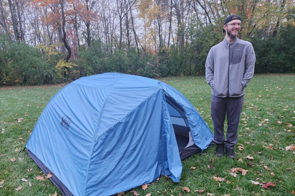 man in gray jacket standing next to a blue tent
