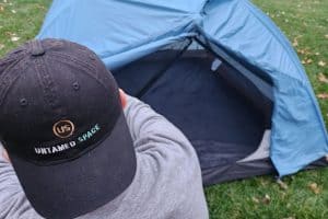 man in black hat putting up a blue tent