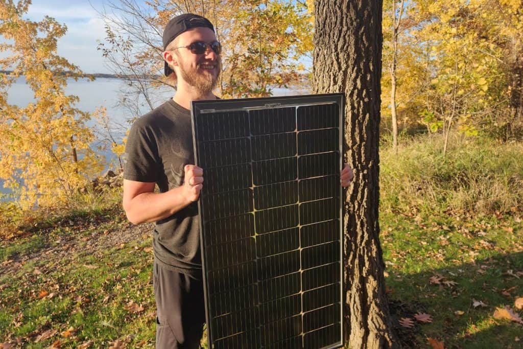 man holding a solar panel by a lake